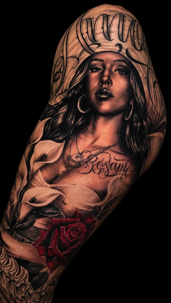 Black and grey chicana realism tattoo with lettering, calla lilies, and a rose, by Sergio Sanchez